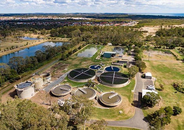 Aerial view of a sewage treatment plant, with circular clarifiers and treatment tanks among trees