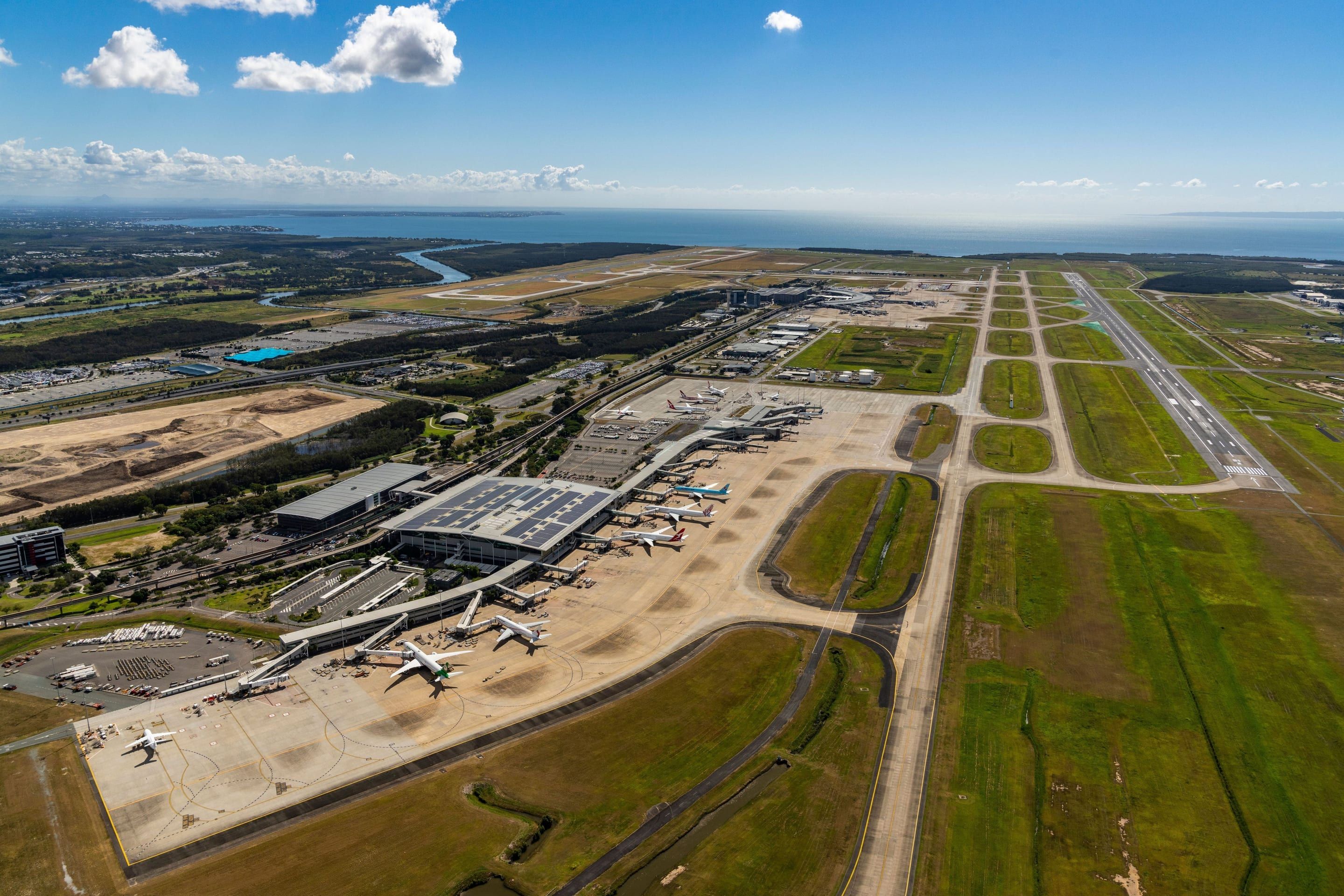 Aerial view of the Brisbane Airport international terminal precinct, with the runways and Moreton Bay beyond